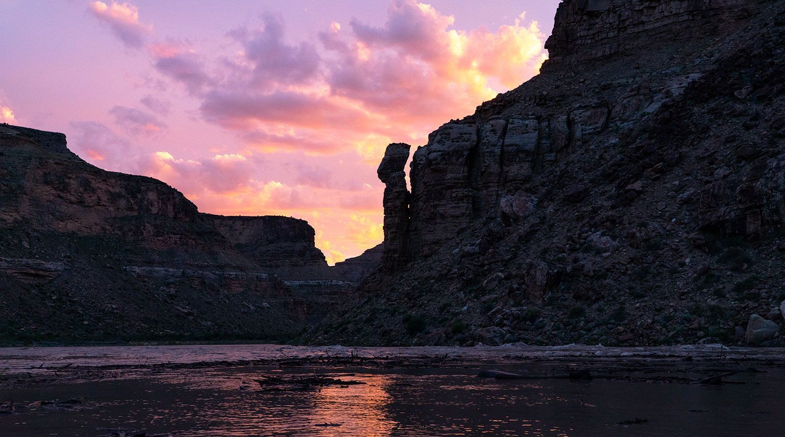 A sunset over a river with a cliff in the foreground.