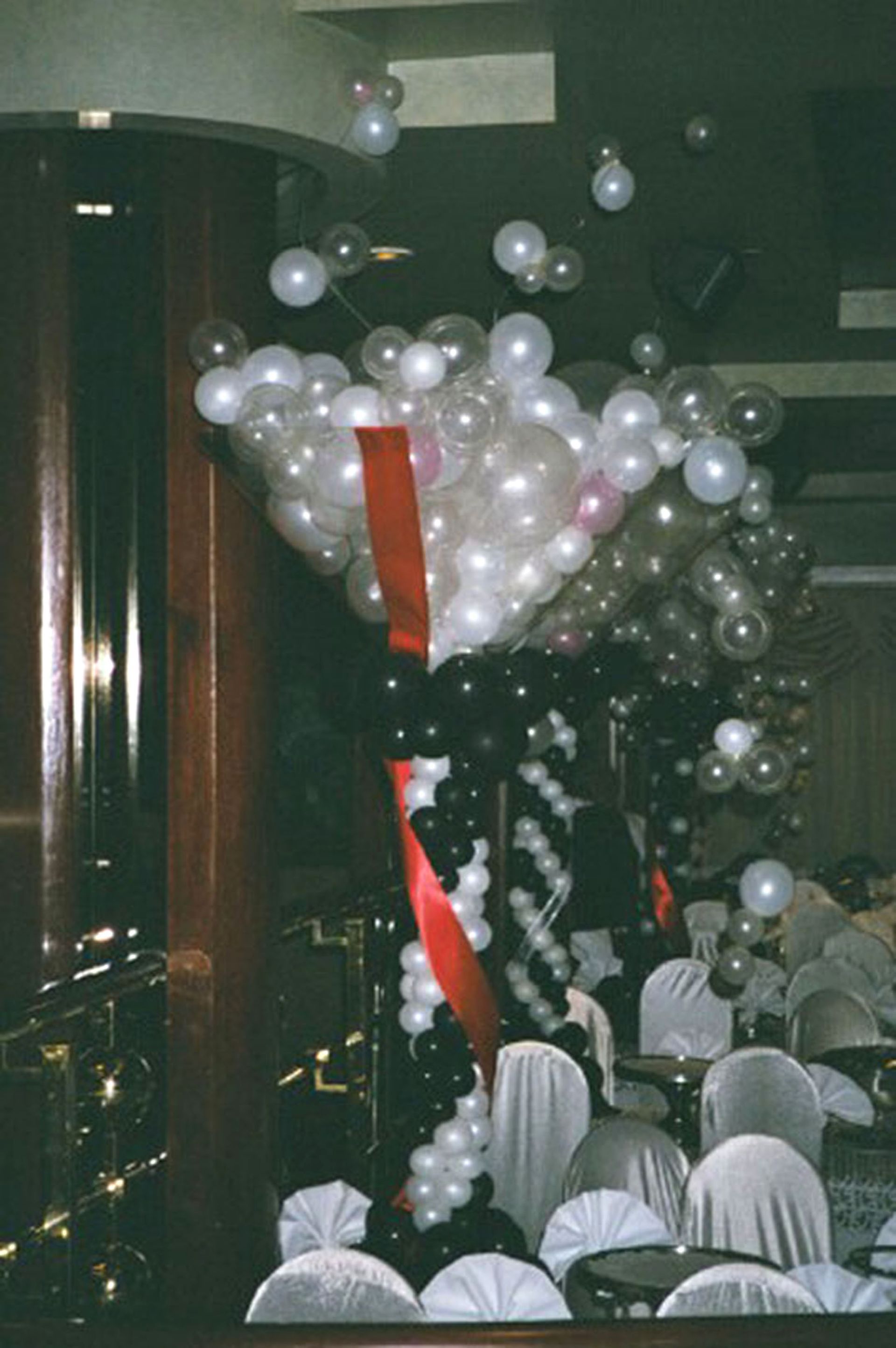 Balloon archway with black, white, and clear balloons, red ribbon, in a banquet hall.