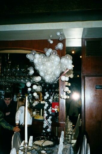 Party with clear and black balloons bursting near a table, bar and people in a dark room.