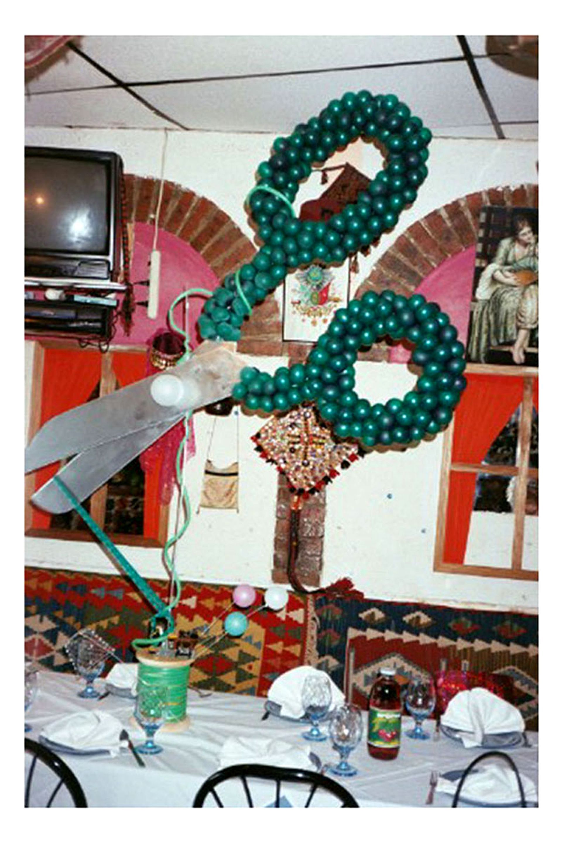 Large green balloon scissors on a table with a white tablecloth, set in a restaurant.