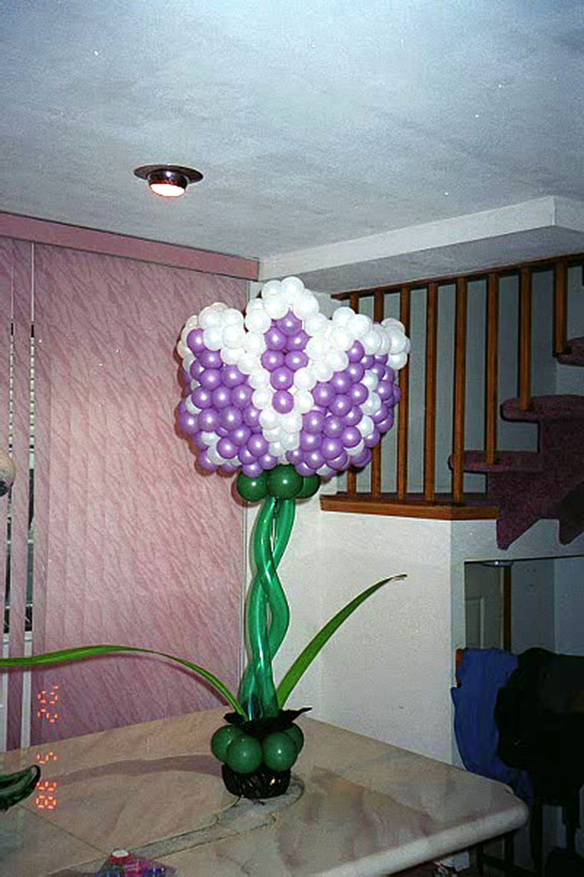 Balloon flower sculpture in white and purple, green stem and leaves on a table.