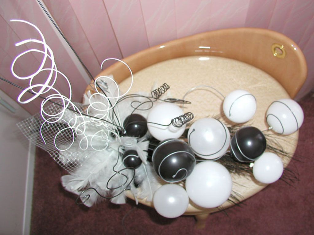 A decorative arrangement of white and black balloons, wire, and fabric, on a light-colored bathtub.