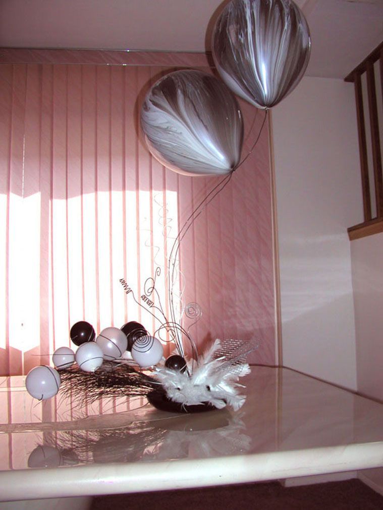 Centerpiece with black and white balloons, orbs, and feathers on a glass table.