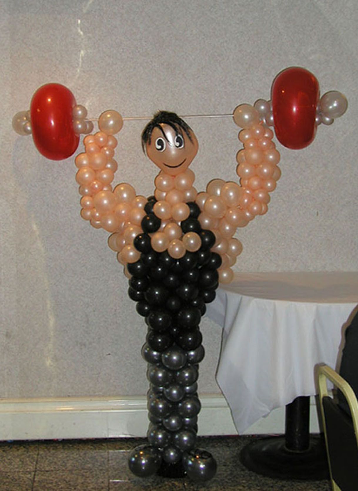Balloon sculpture of a weightlifter with red weights. Black and peach-colored balloons make up the body.