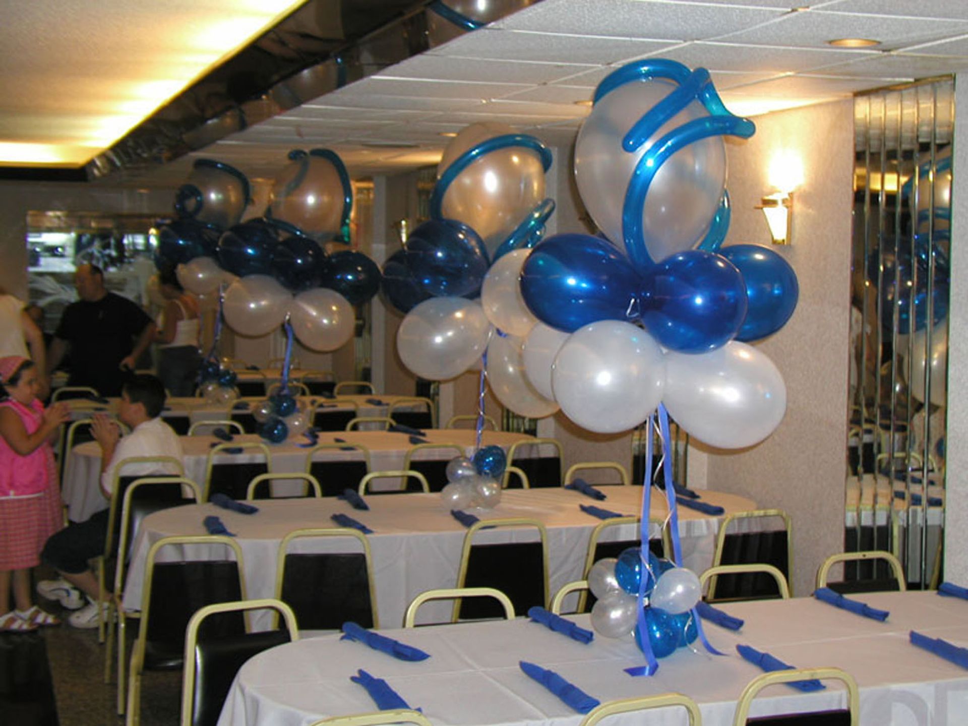 Party room with tables set for a celebration. Balloon centerpieces in blue, white, and silver.