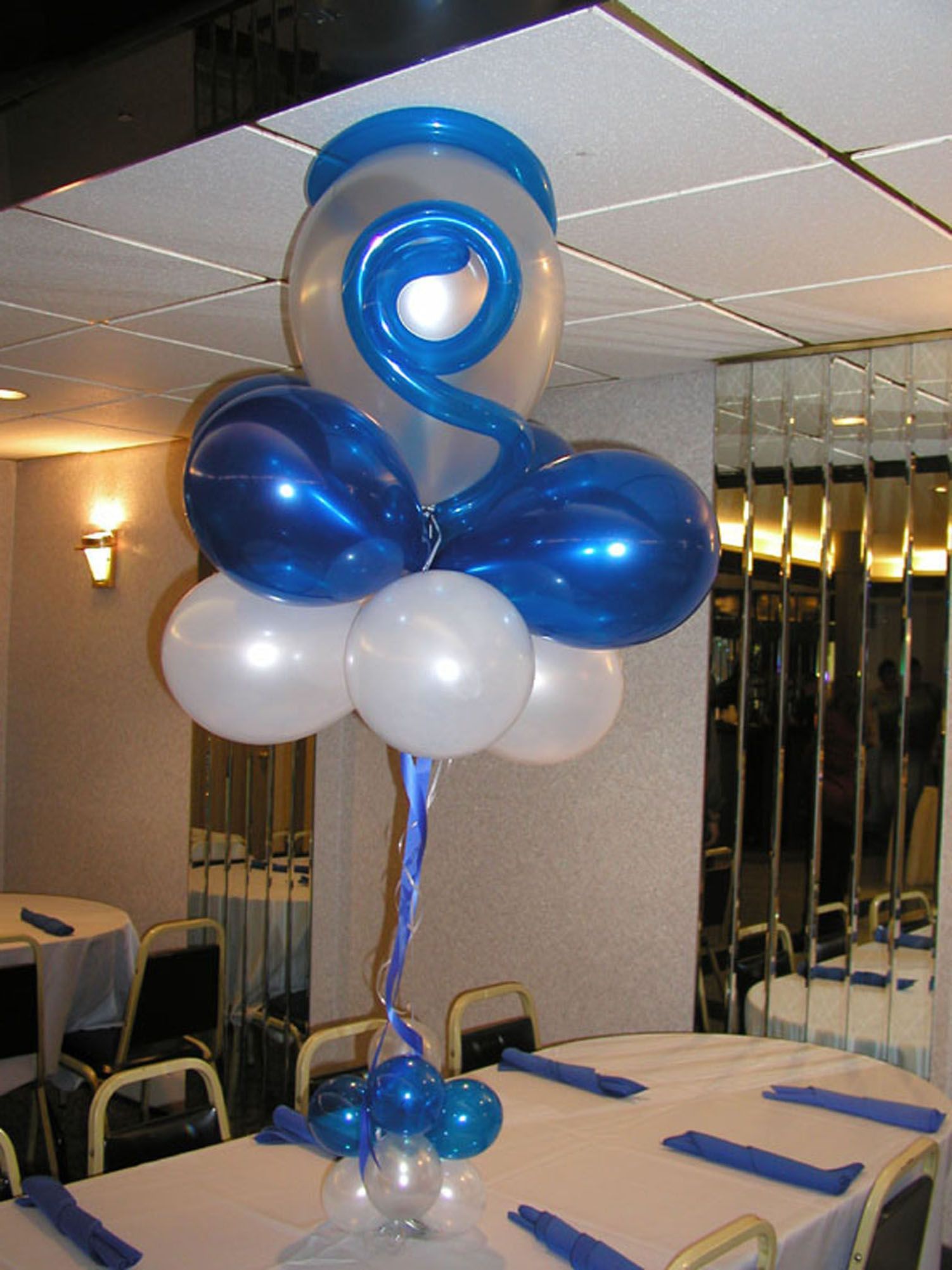 Balloon centerpiece on a table, featuring blue, white, and clear balloons. Restaurant setting.