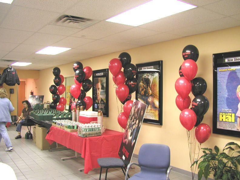 Red and black balloons decorate a room with movie posters, refreshments on a table, and people present.