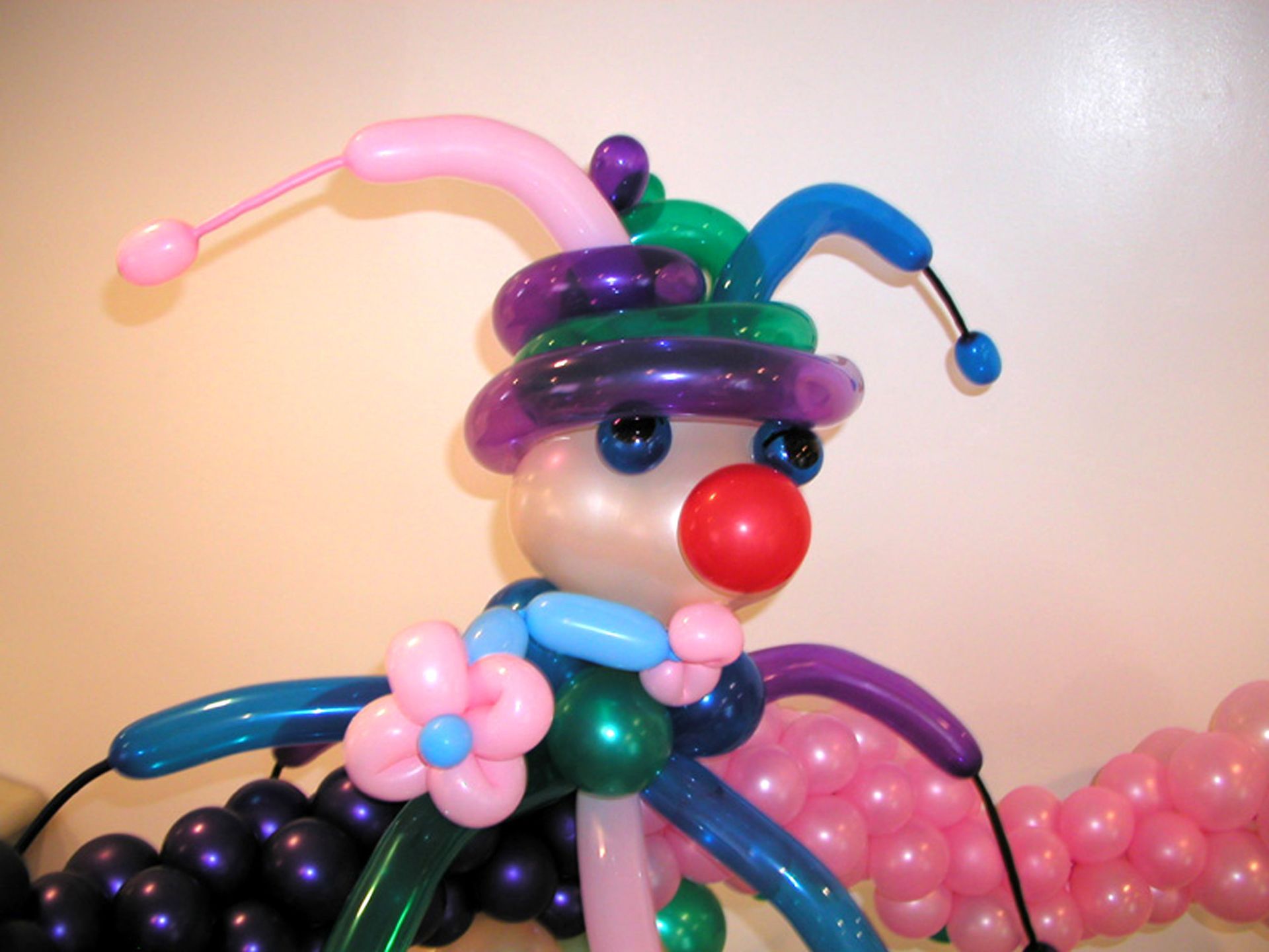 A colorful clown sculpture made of balloons, featuring a red nose, jester hat, and floral decorations.