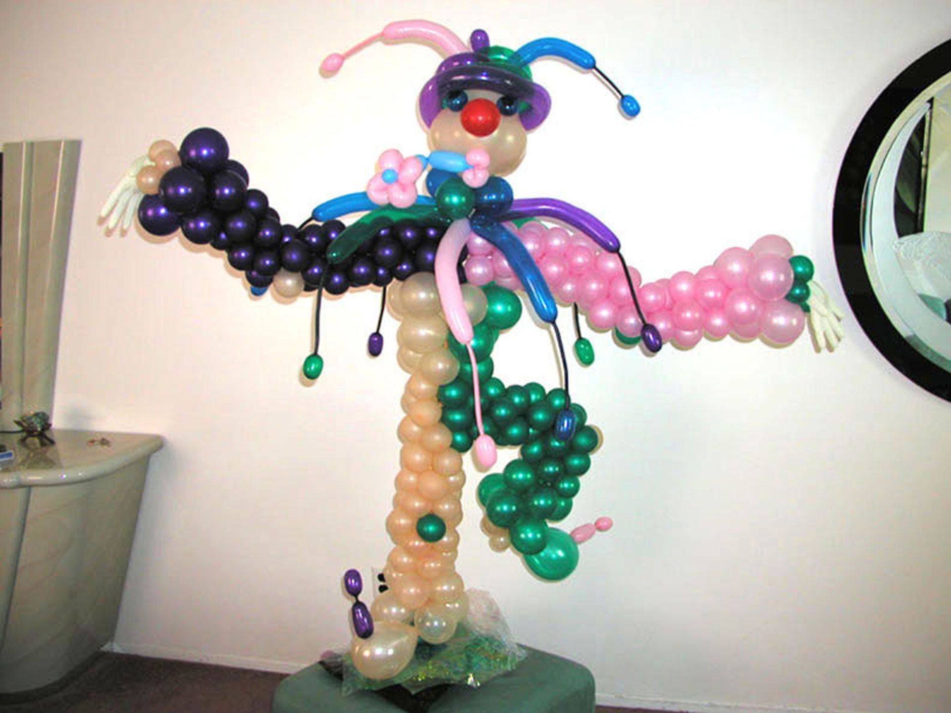 Balloon sculpture of a colorful clown with outstretched arms, standing indoors.