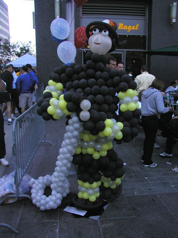 Firefighter sculpture made of black, yellow, and white balloons, standing near a bagel shop.