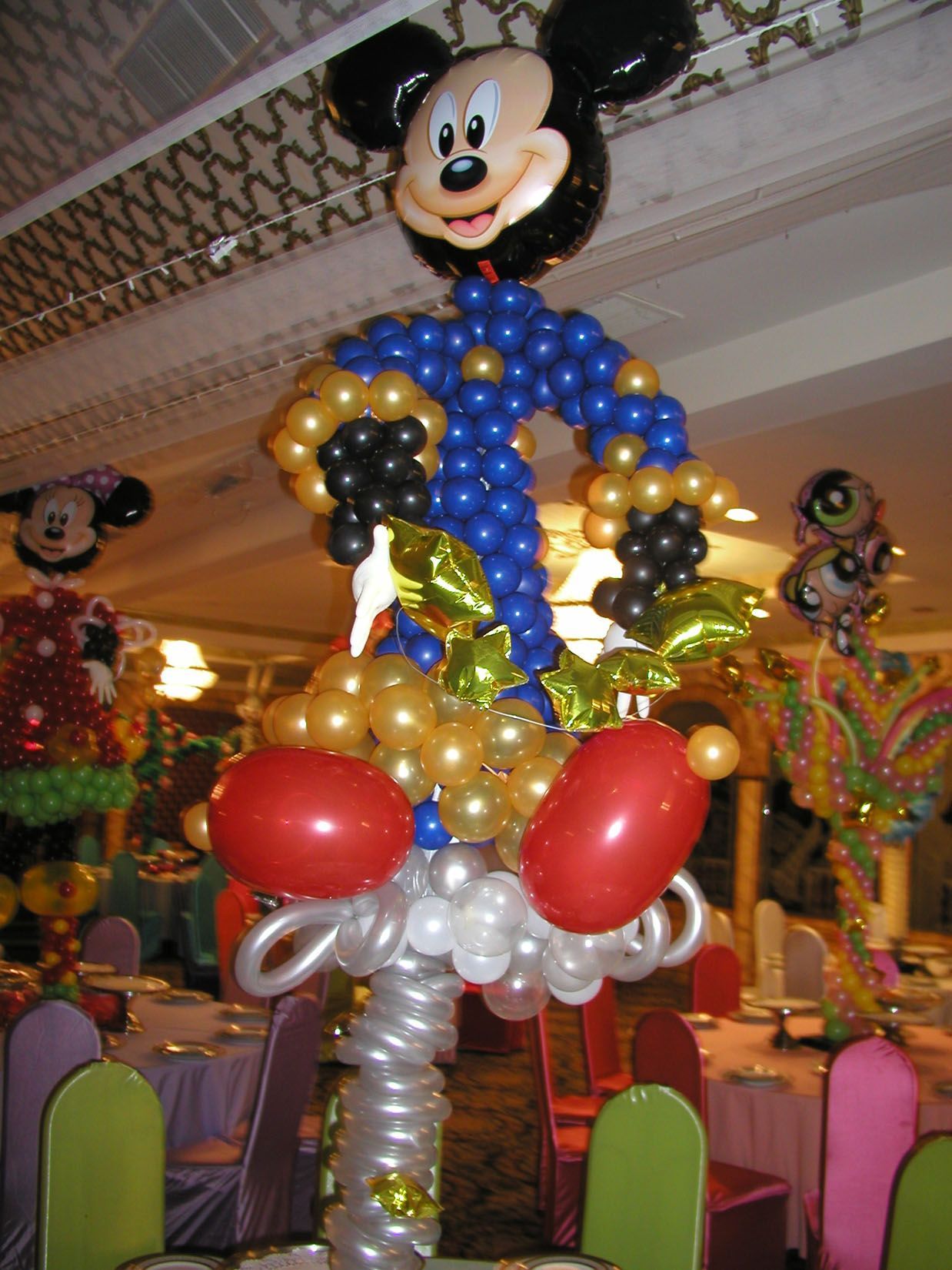 Mickey Mouse balloon sculpture at a party, blue, gold, red, and black balloons, indoors.
