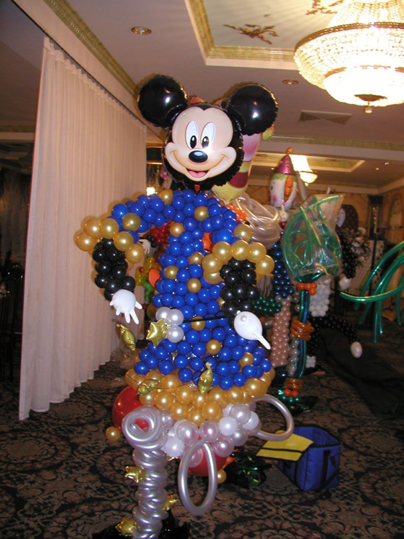 Mickey Mouse balloon sculpture in blue and gold robes, standing in a decorated room.