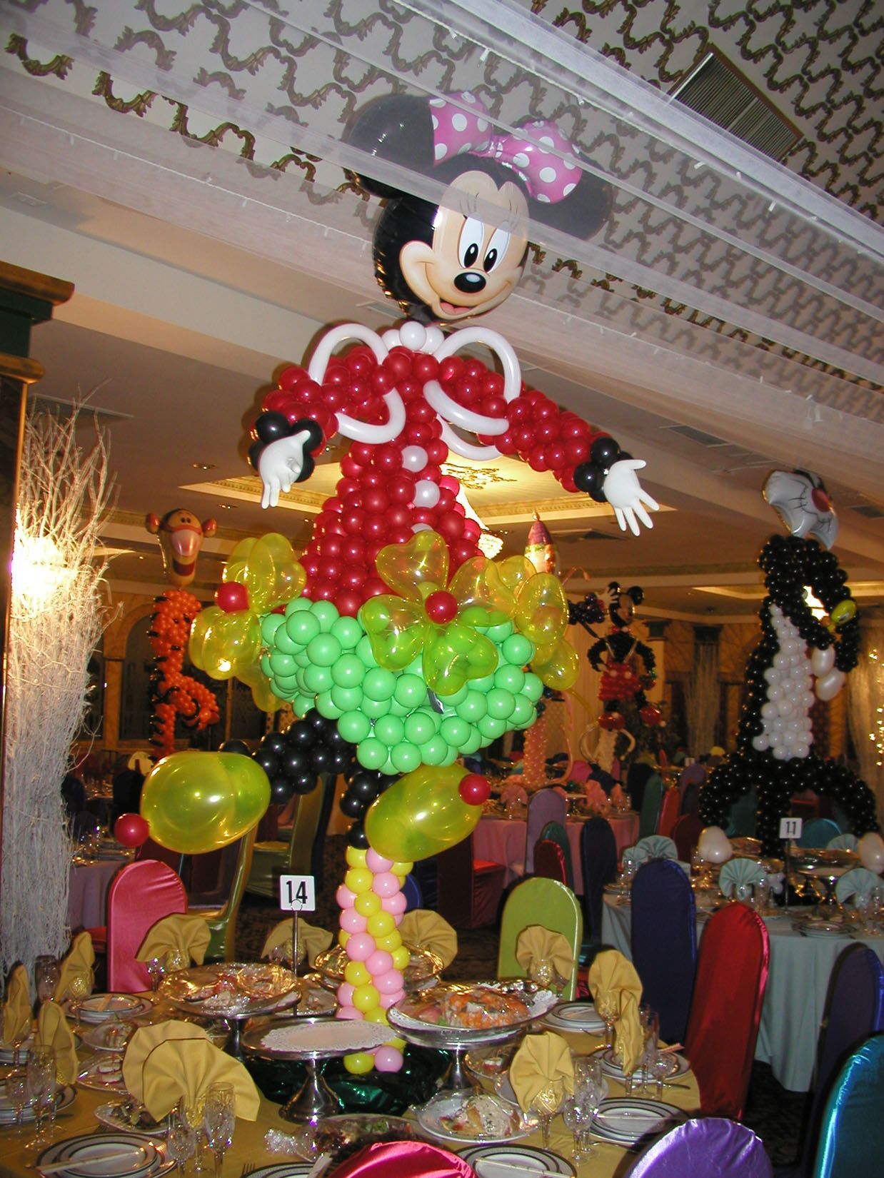 Balloon sculpture of Minnie Mouse over a party table, surrounded by other balloon decorations.