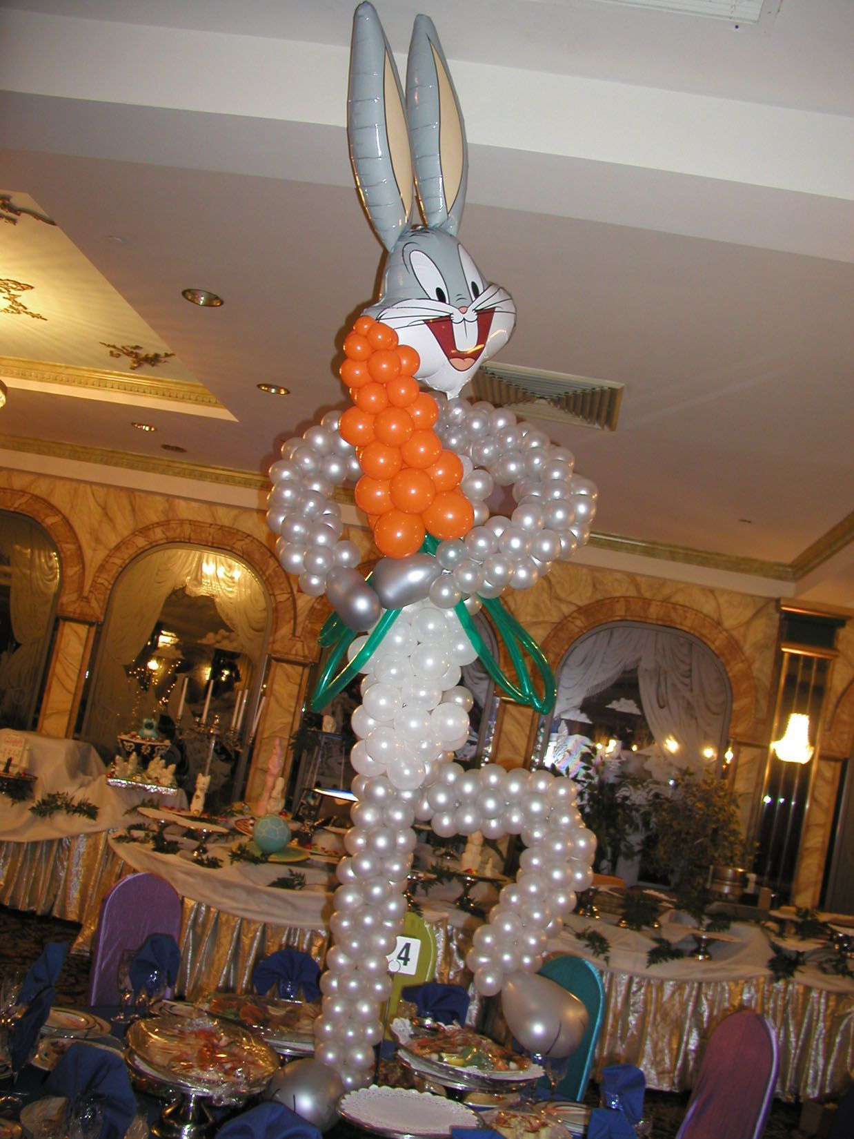 Bugs Bunny balloon sculpture in a dining room, holding a carrot, wearing a green vest.