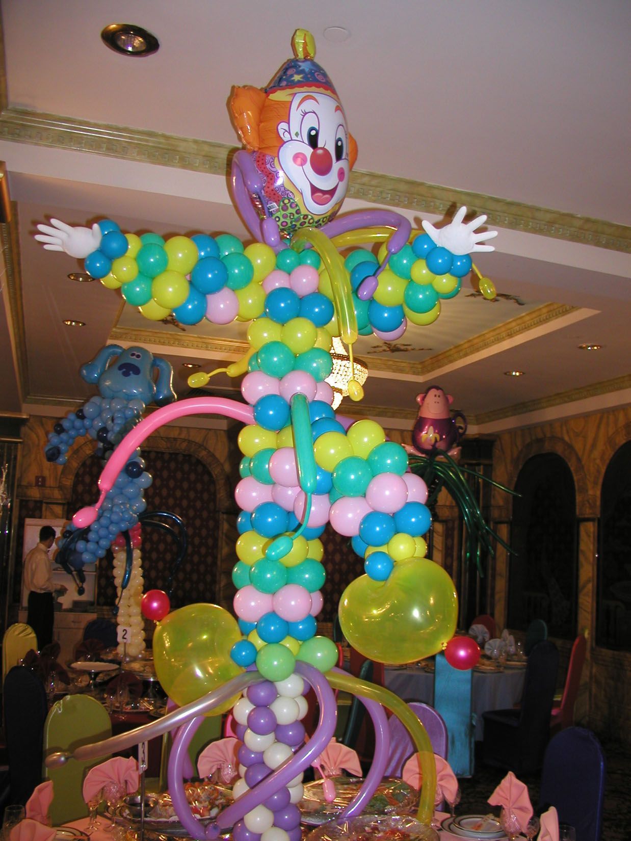 Clown sculpture made of colorful balloons, standing on a table in a decorated room.