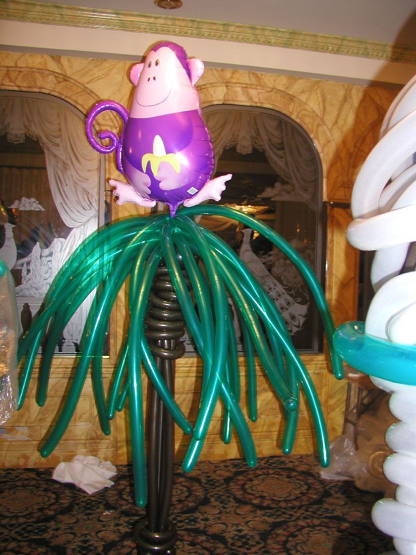Balloon sculpture of a purple monkey with banana on green palm tree made of balloons.