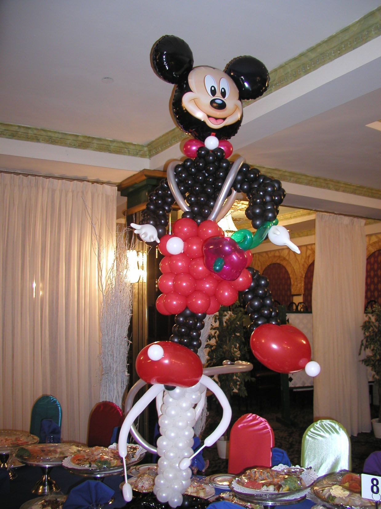 Mickey Mouse balloon sculpture with black, red, and white balloons stands on a table at an event.