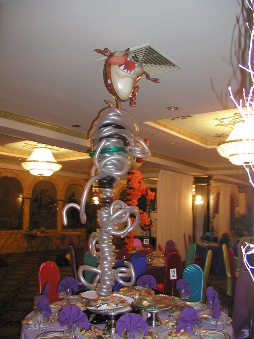 A balloon sculpture of an owl atop a table, featuring swirling silver, black, and green balloons; banquet hall setting.