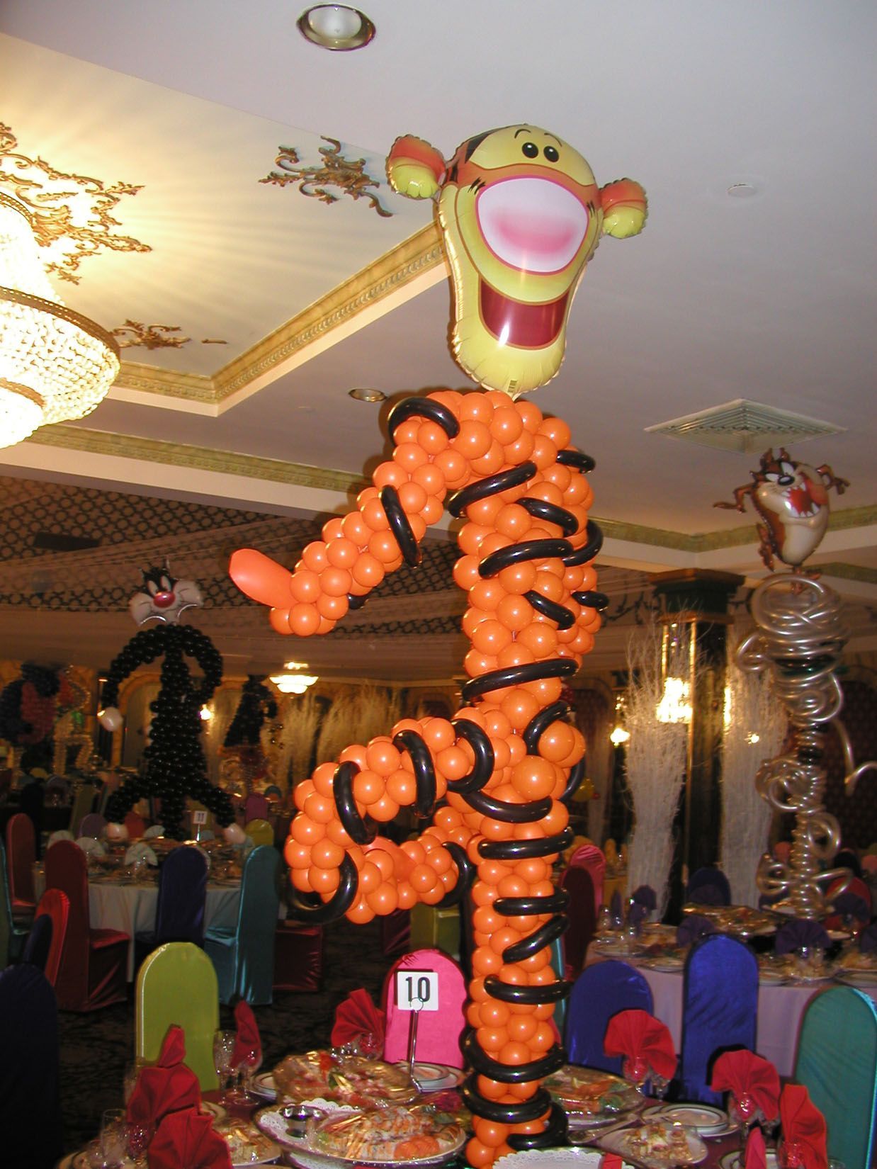 Balloon sculpture of Tigger, orange and black balloons, with Tigger's face at top. Party setting.