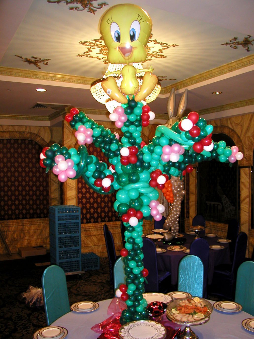 Tweety Bird balloon centerpiece on a dining table; green, red, pink balloons create a tree shape.