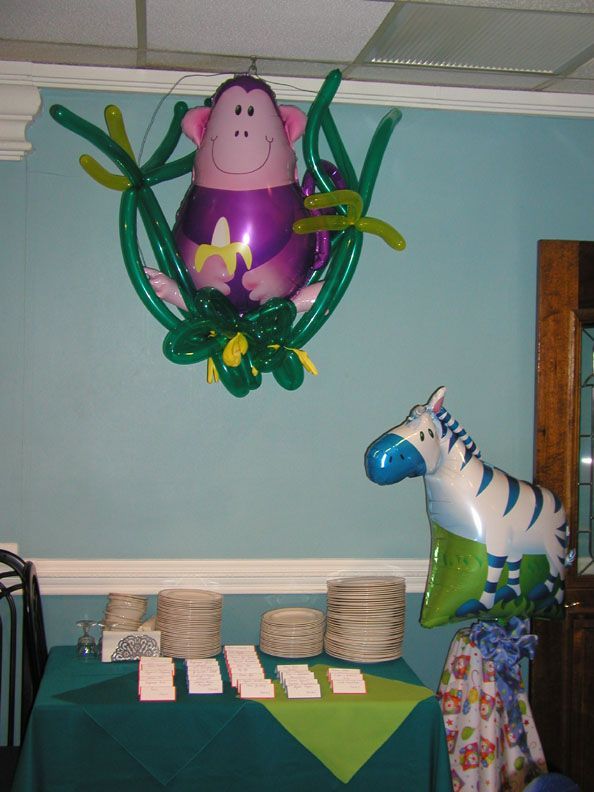 A jungle-themed party decoration with a monkey and zebra balloon, over a table with plates and napkins.