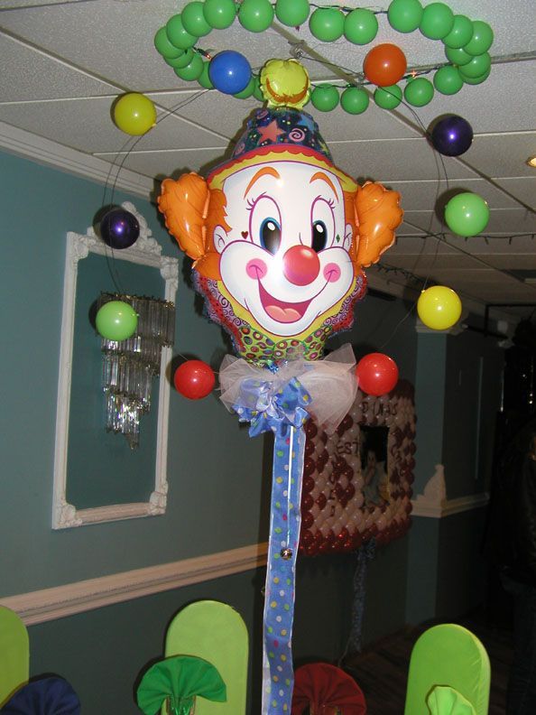 Clown balloon centerpiece with colorful balloons hanging from a green circular structure in a room with teal walls.