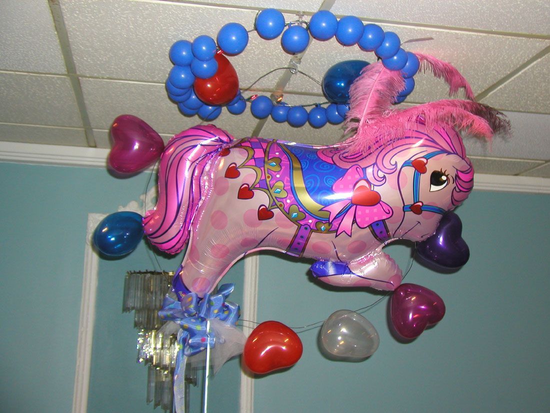 Pink pony balloon decoration with heart-shaped balloons, blue accents, and a blue balloon wreath hanging from a ceiling.