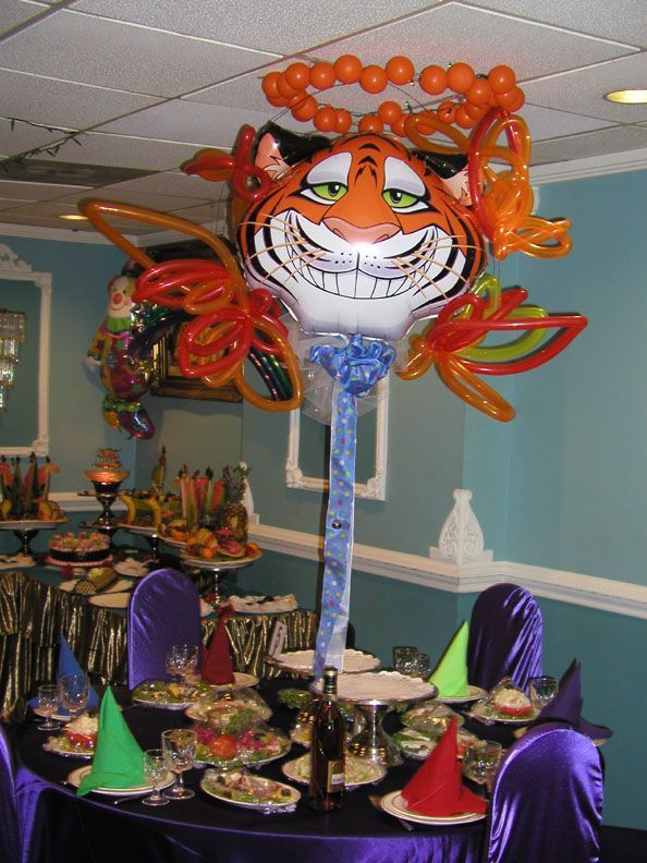 Tiger balloon centerpiece over a decorated table with food and purple chairs. Orange, blue, and white colors dominate.