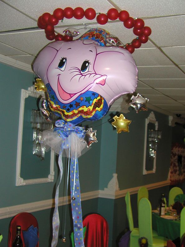 A Dumbo balloon decoration with a red balloon halo, dangling ribbons, and star-shaped balloons, indoors.