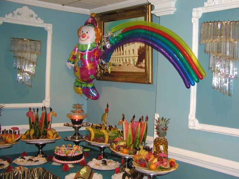 Clown balloon with rainbow over dessert buffet in a room with ornate wall sconces and a painting.