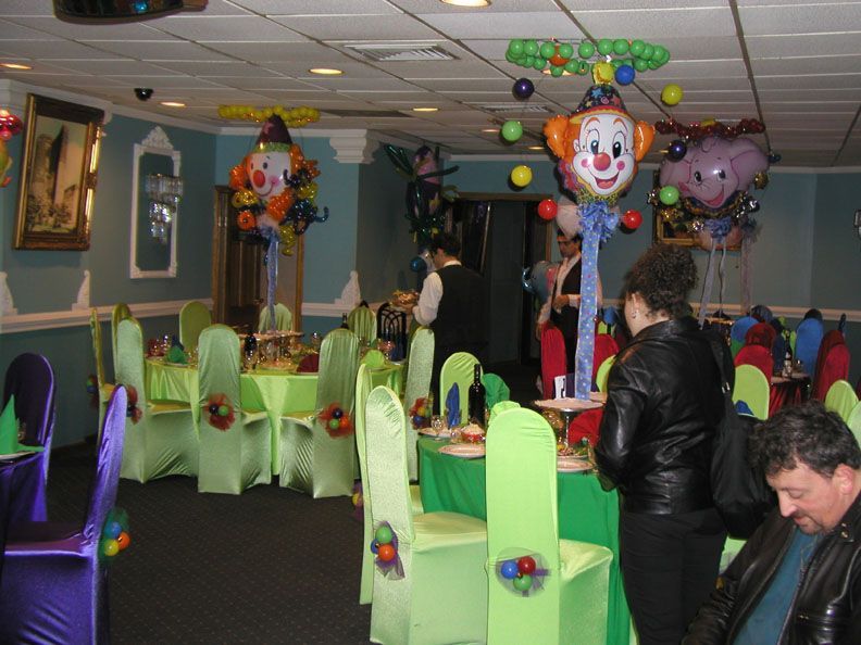 Party room decorated with clown balloons, green and purple chairs, and people attending.