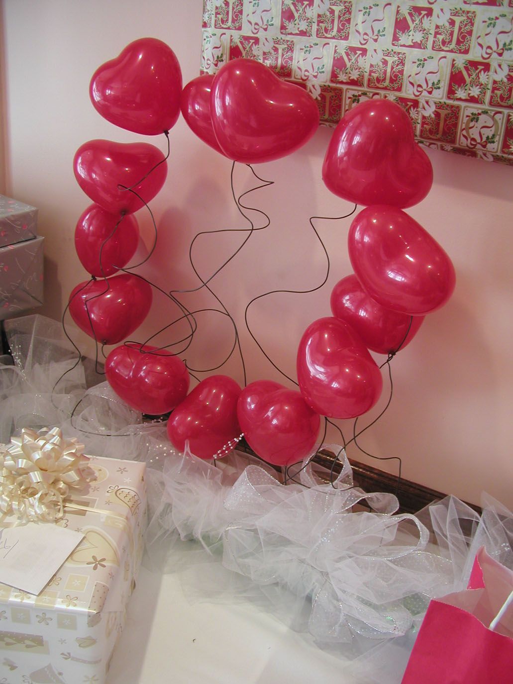 Red heart-shaped balloons form a circle, displayed with presents and sheer white fabric.