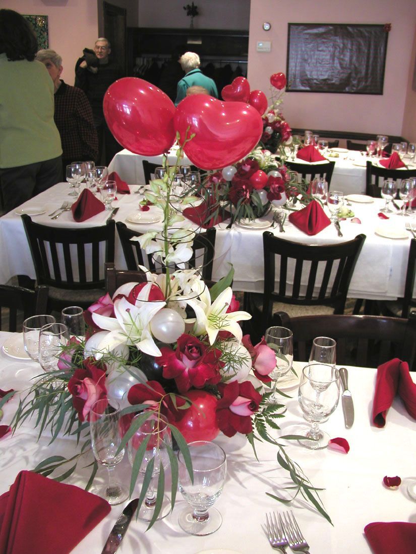 Tables set for a celebration, decorated with red and white flowers and heart-shaped balloons.