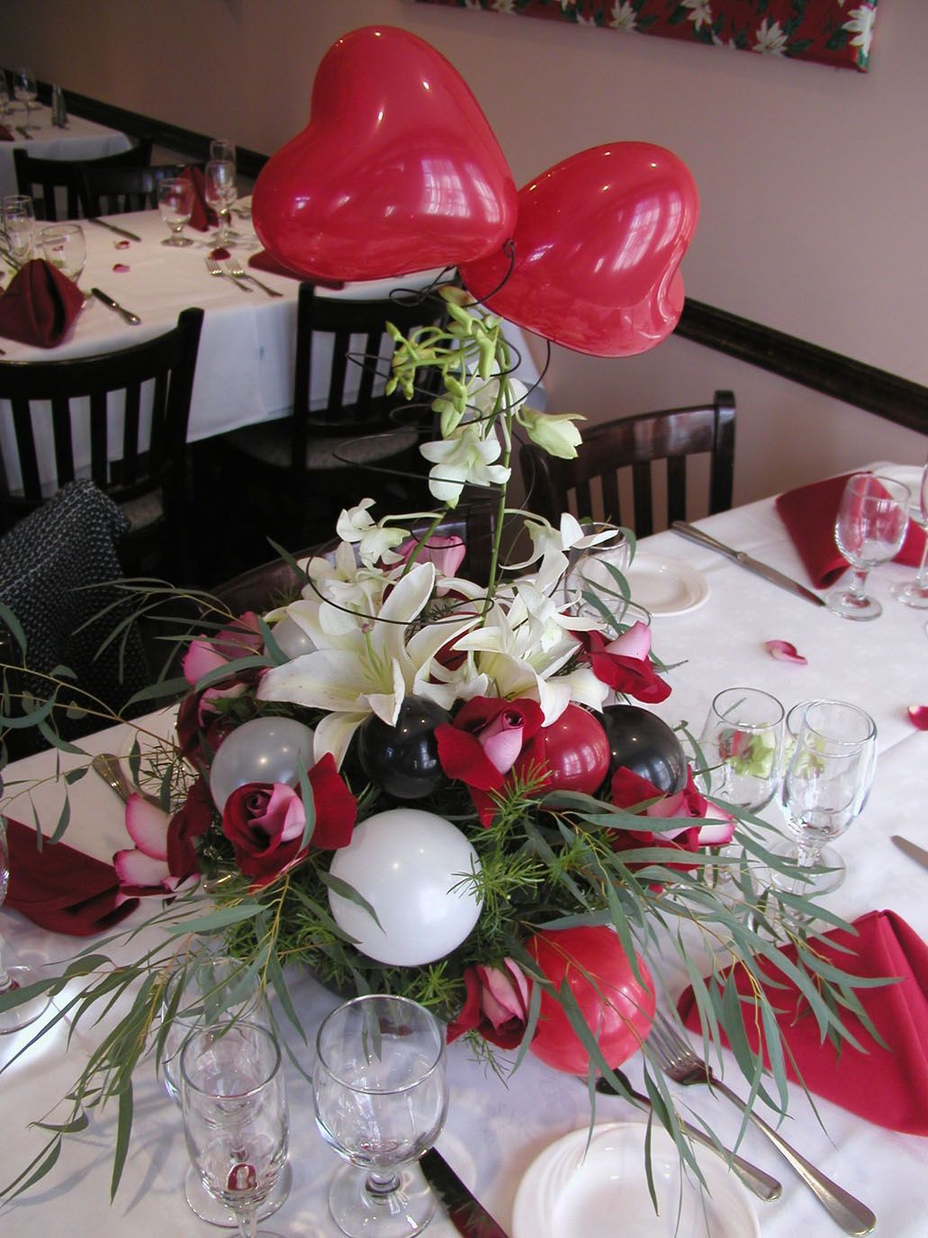 Table centerpiece with heart balloons, flowers, and decorations for a special event.