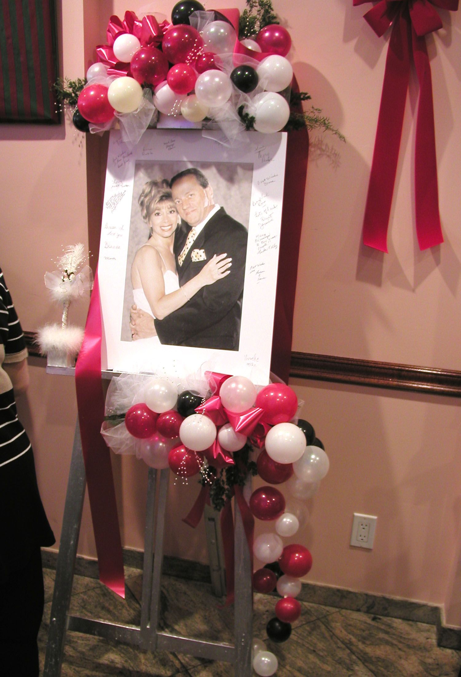 Wedding photo on easel decorated with red, white, and black balloons, inside a venue.