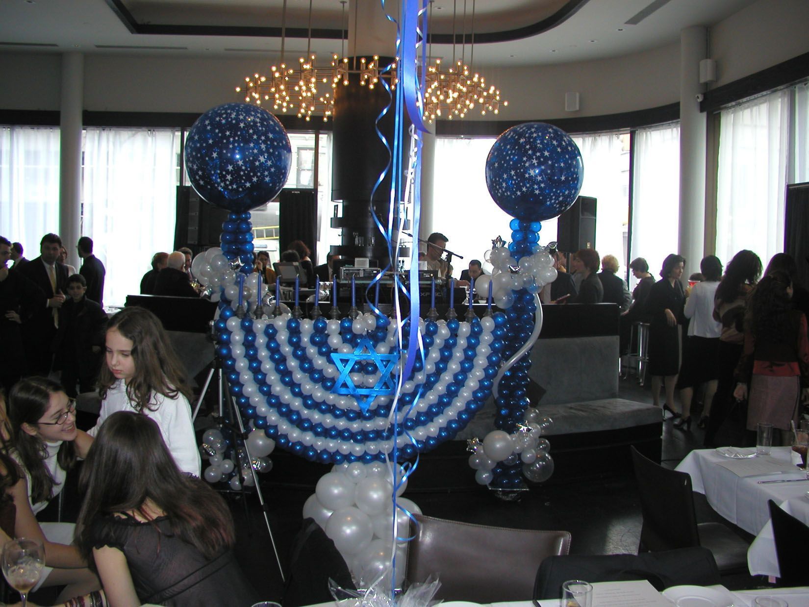 Balloon menorah centerpiece at an event; people in formal wear, dark blue and silver decor.