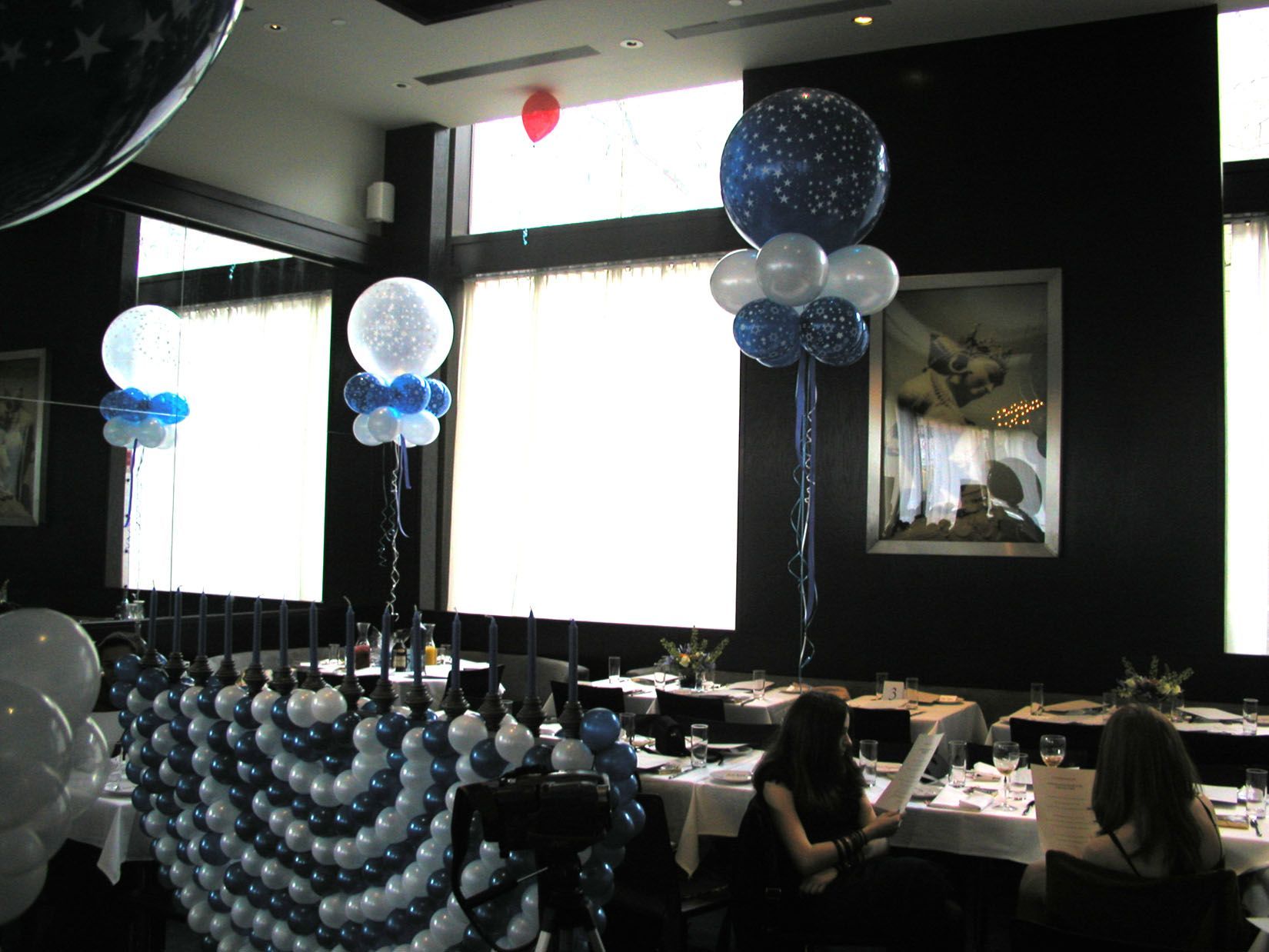 Restaurant decorated with blue and white balloons; two people at a table, one reading.