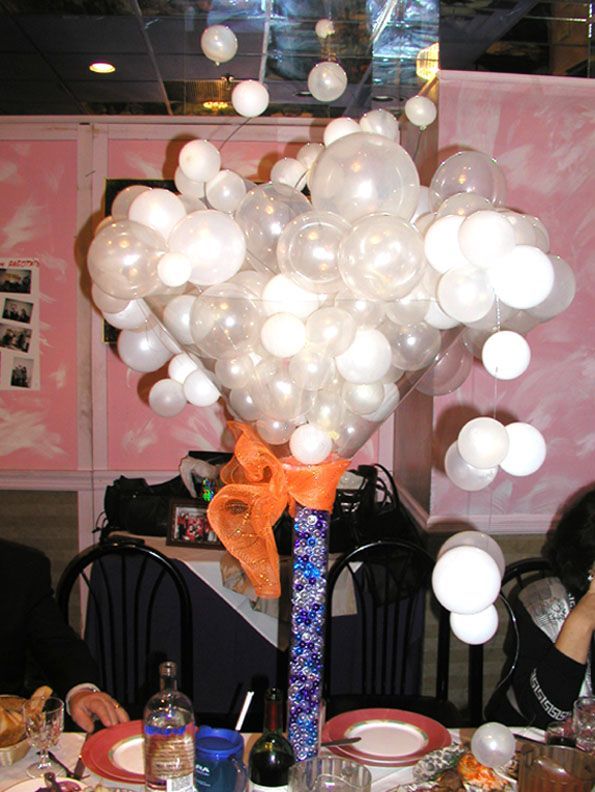 Centerpiece with white and clear balloons, orange bow, and blue vase on a table.