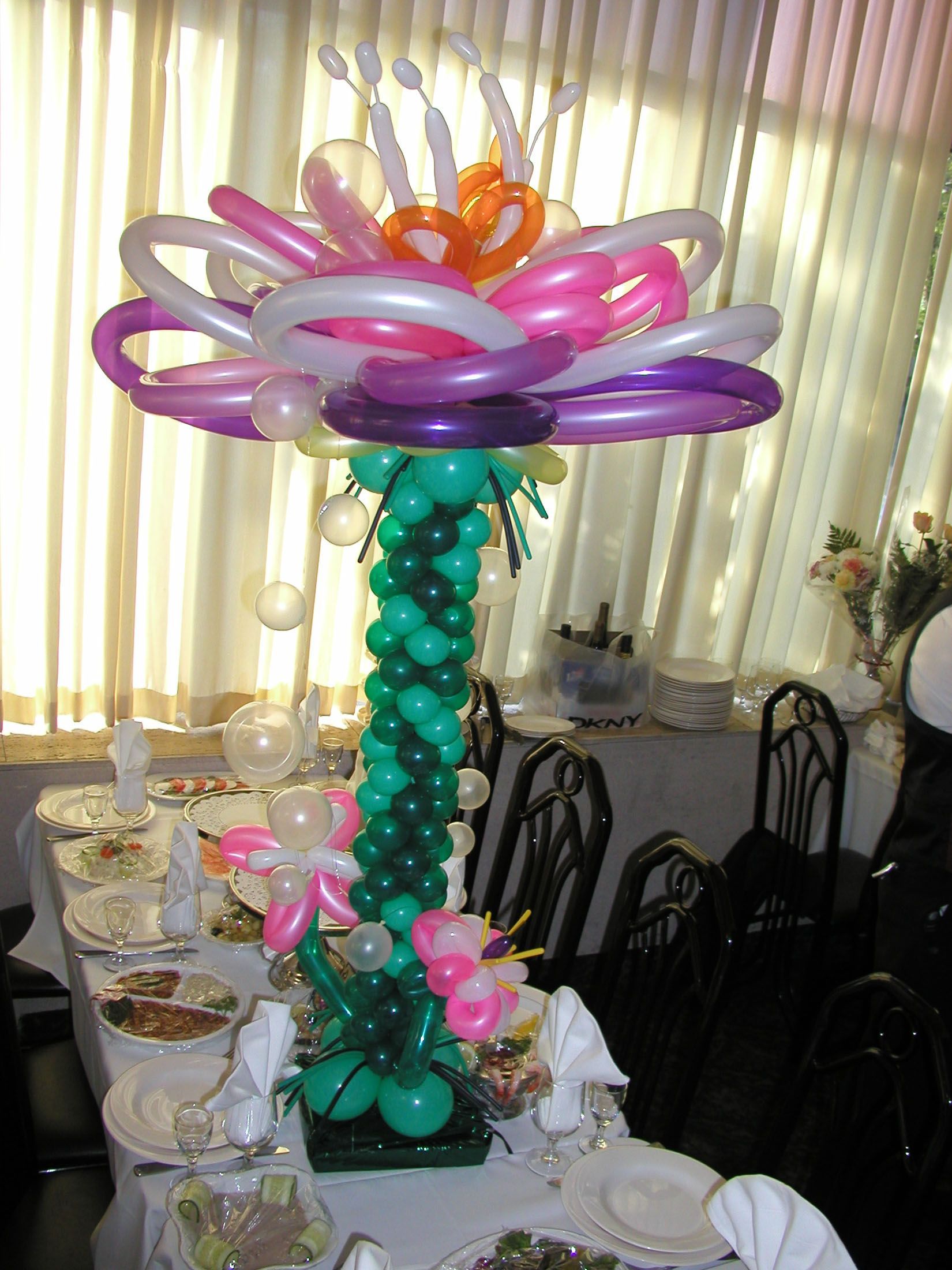 Balloon flower centerpiece on a table with food, featuring various colors and shapes.