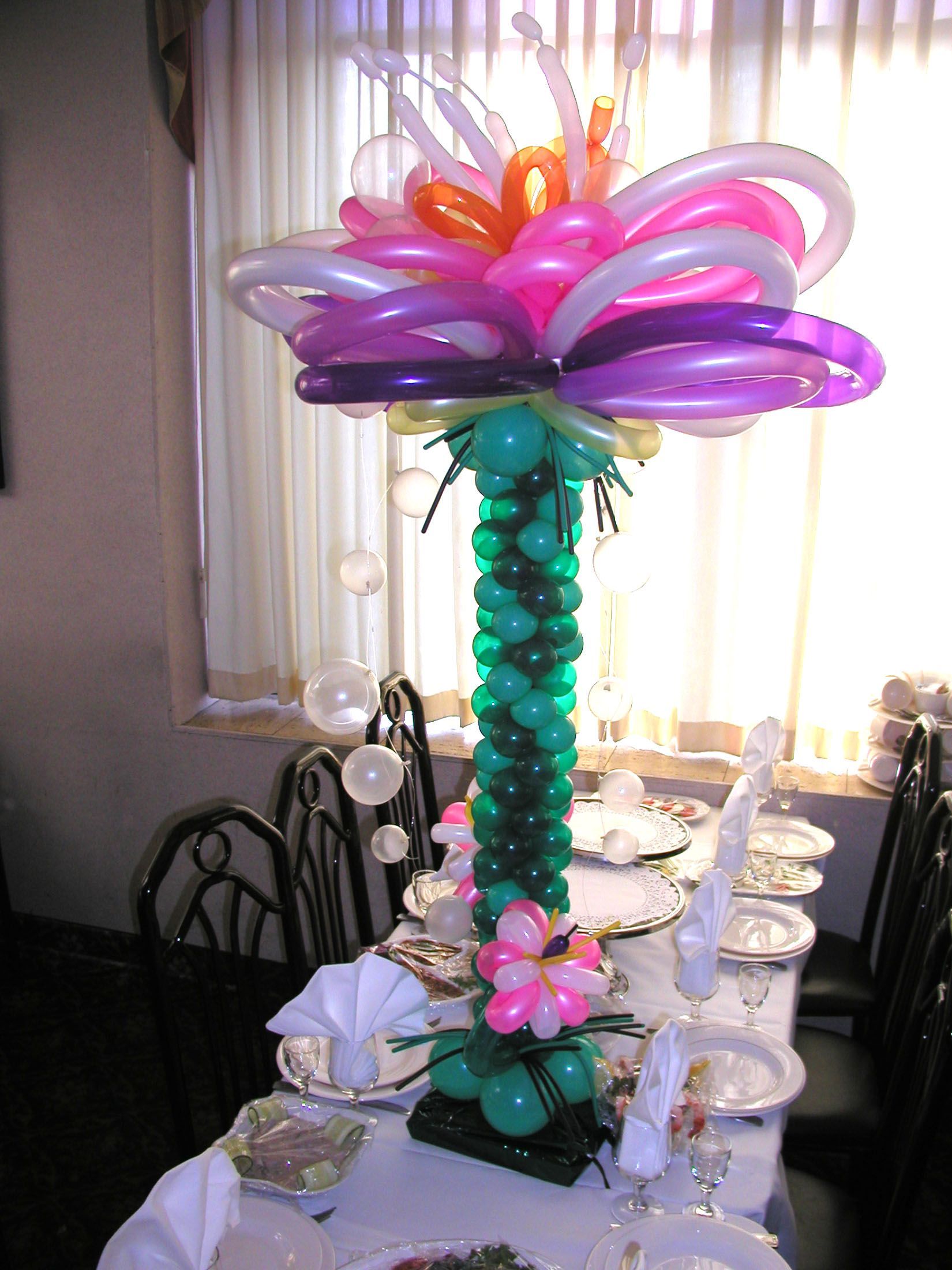 Balloon flower centerpiece on a table, with a tall green stem, and colorful petals.