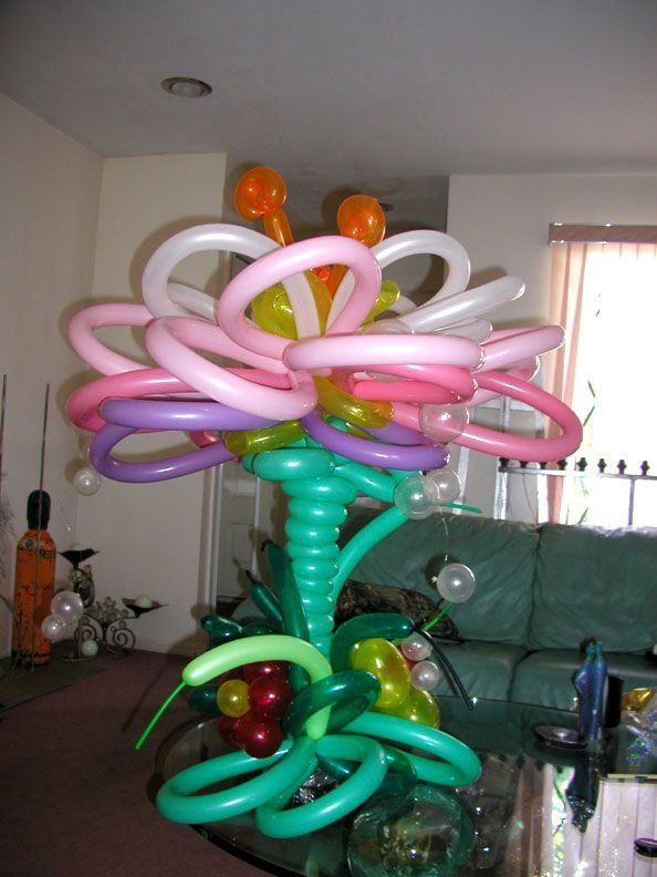 Balloon sculpture of a colorful flower arrangement on a table, with green, pink, and yellow elements.