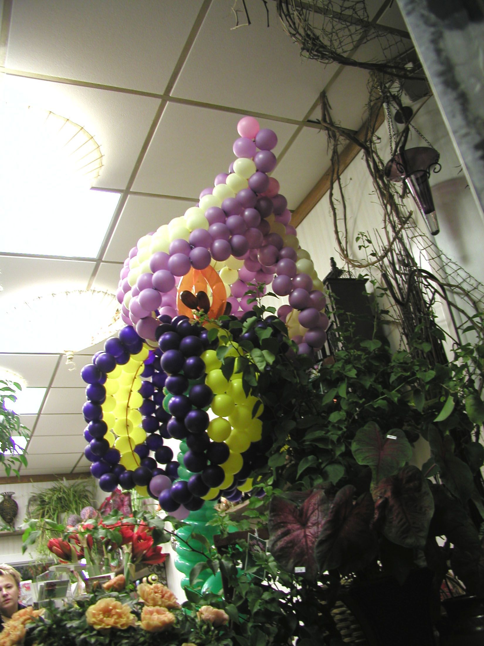 A large balloon sculpture in a flower shop, shaped like a whimsical house. Various colors and greenery surround it.