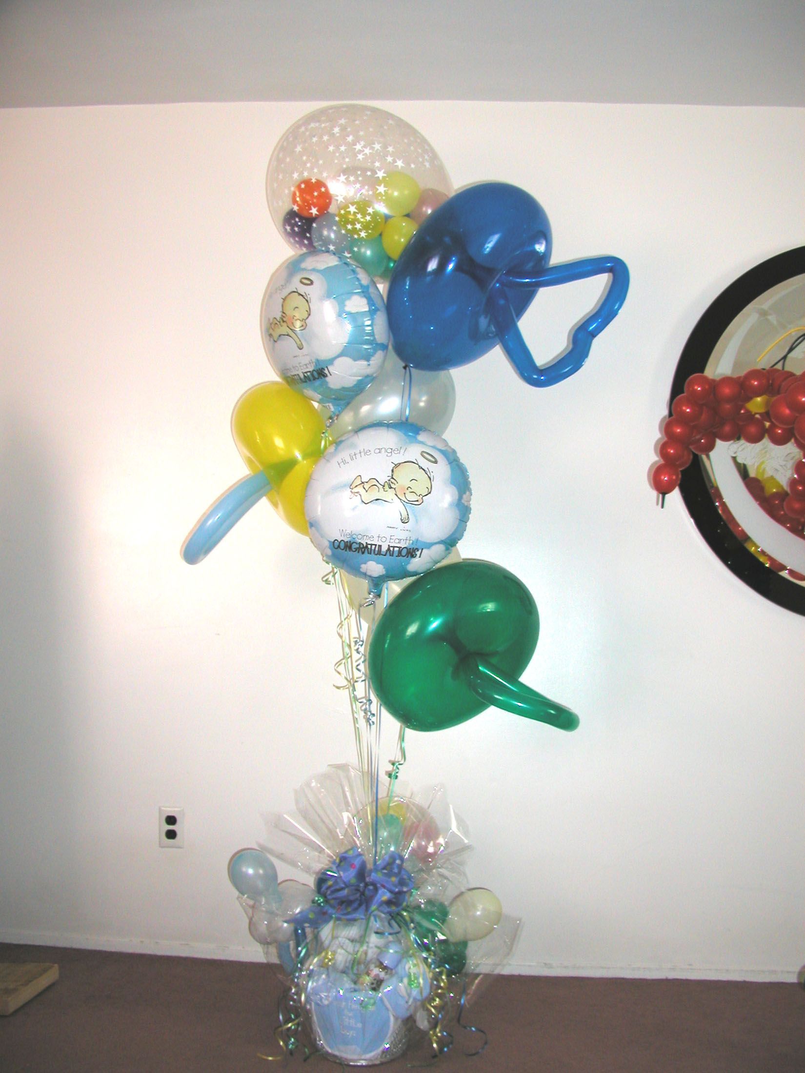 Balloon bouquet with baby-themed balloons in various colors, including blue, yellow, and green, atop a floral arrangement.