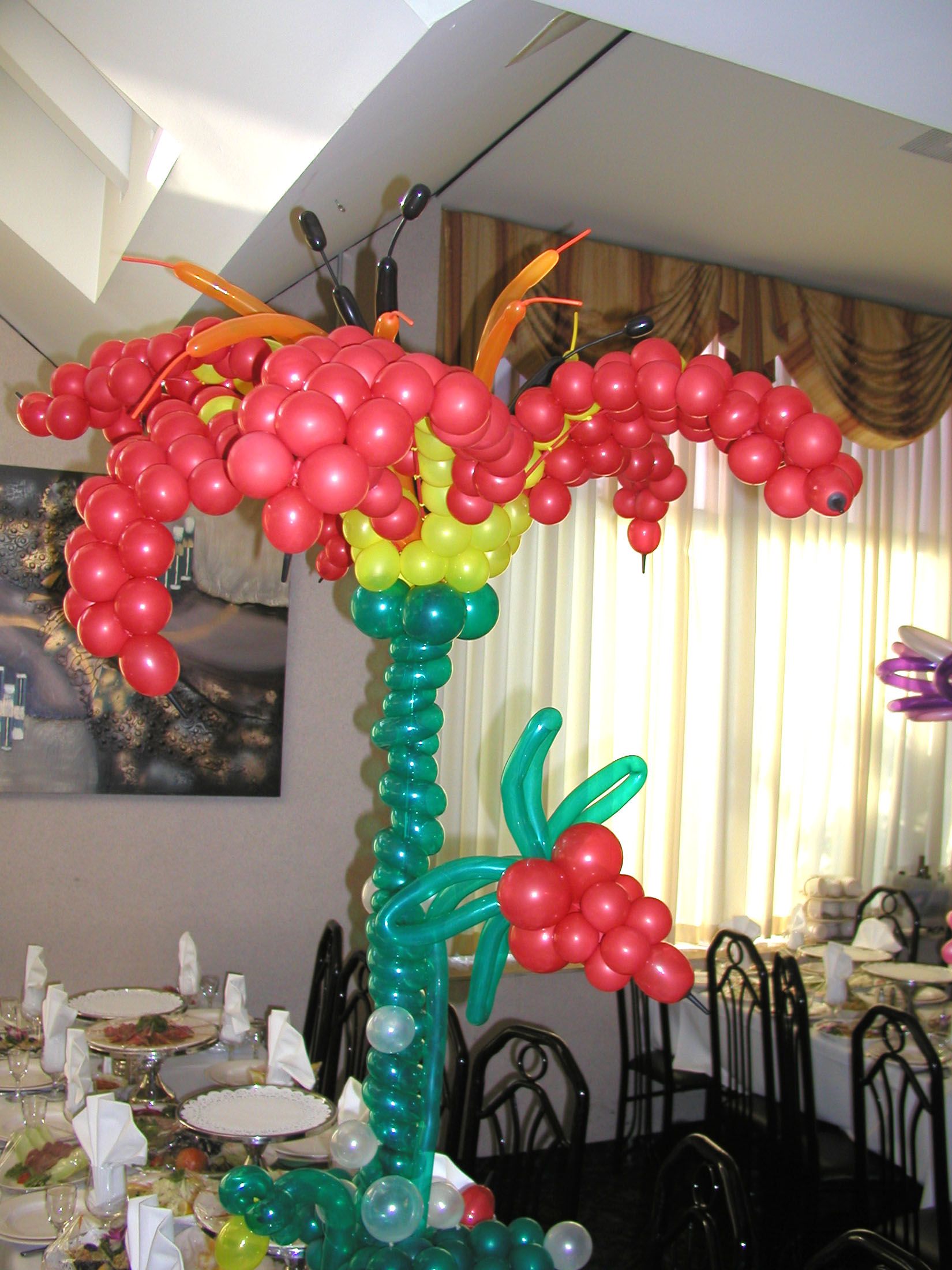 Balloon flower decoration at a party; red and yellow blossoms, green stem and leaves.