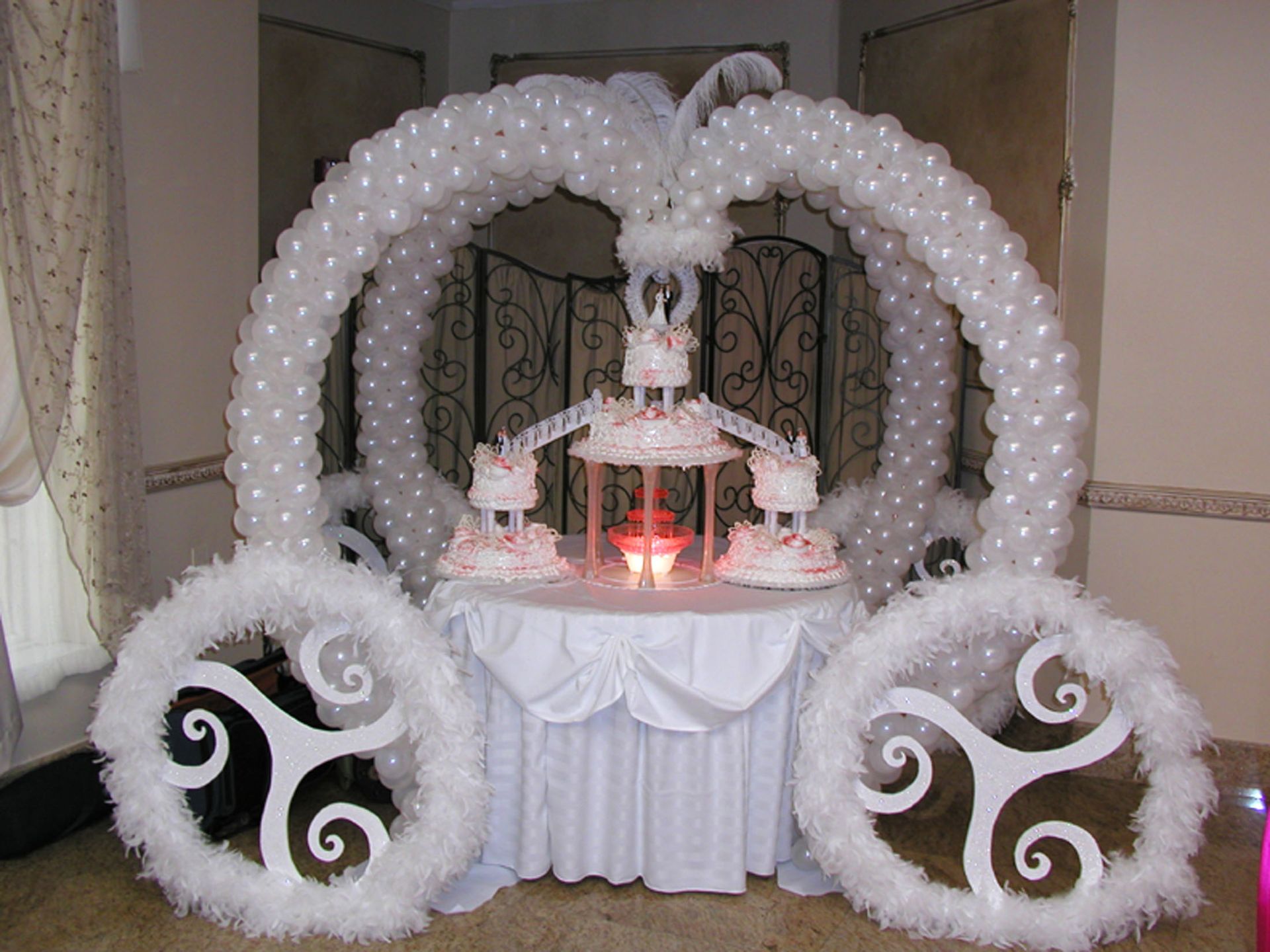 Cinderella carriage cake display, white balloons, wheels, and table setting with cake and candles.
