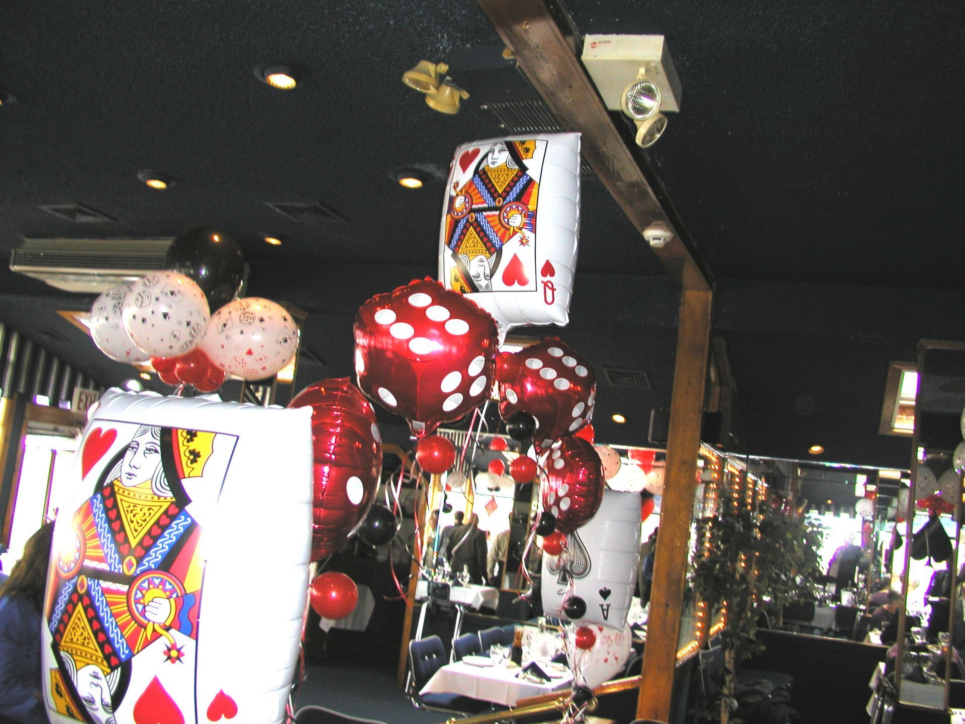 Casino-themed party decor with playing card and dice balloons. Black ceiling, people in the background.