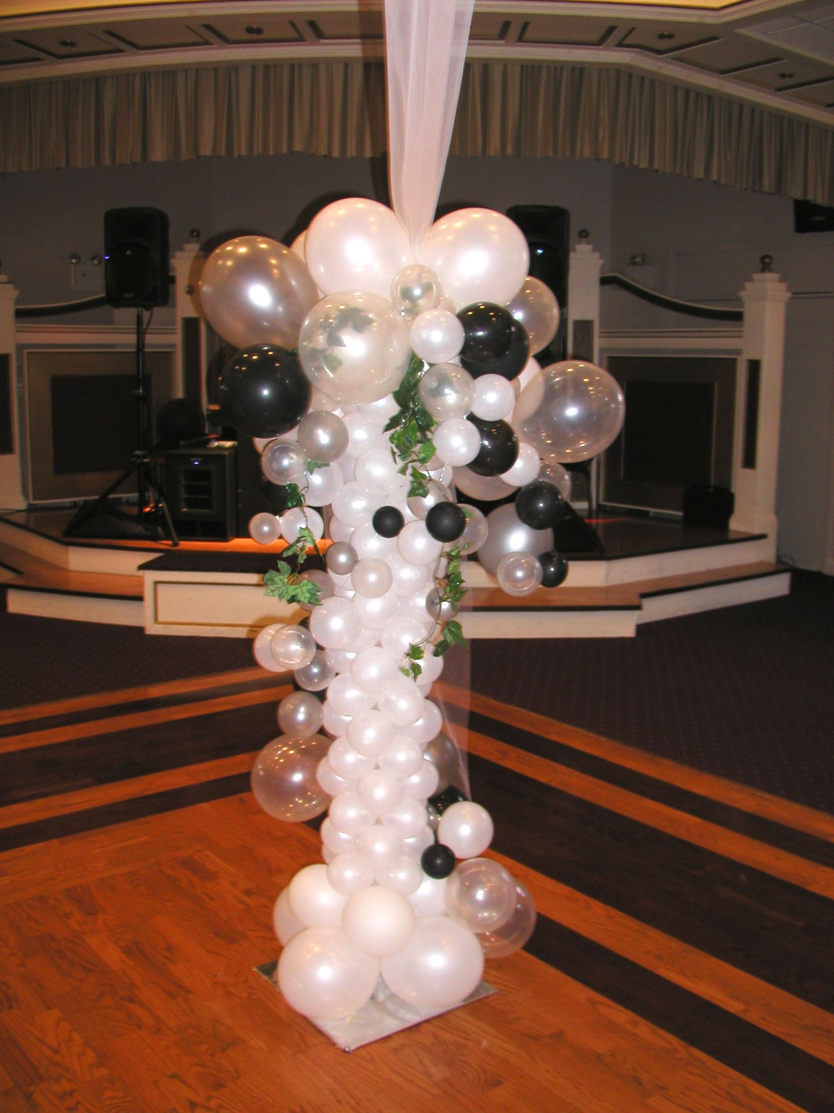 Balloon column decoration in a ballroom, featuring white, silver, and black balloons, with greenery.