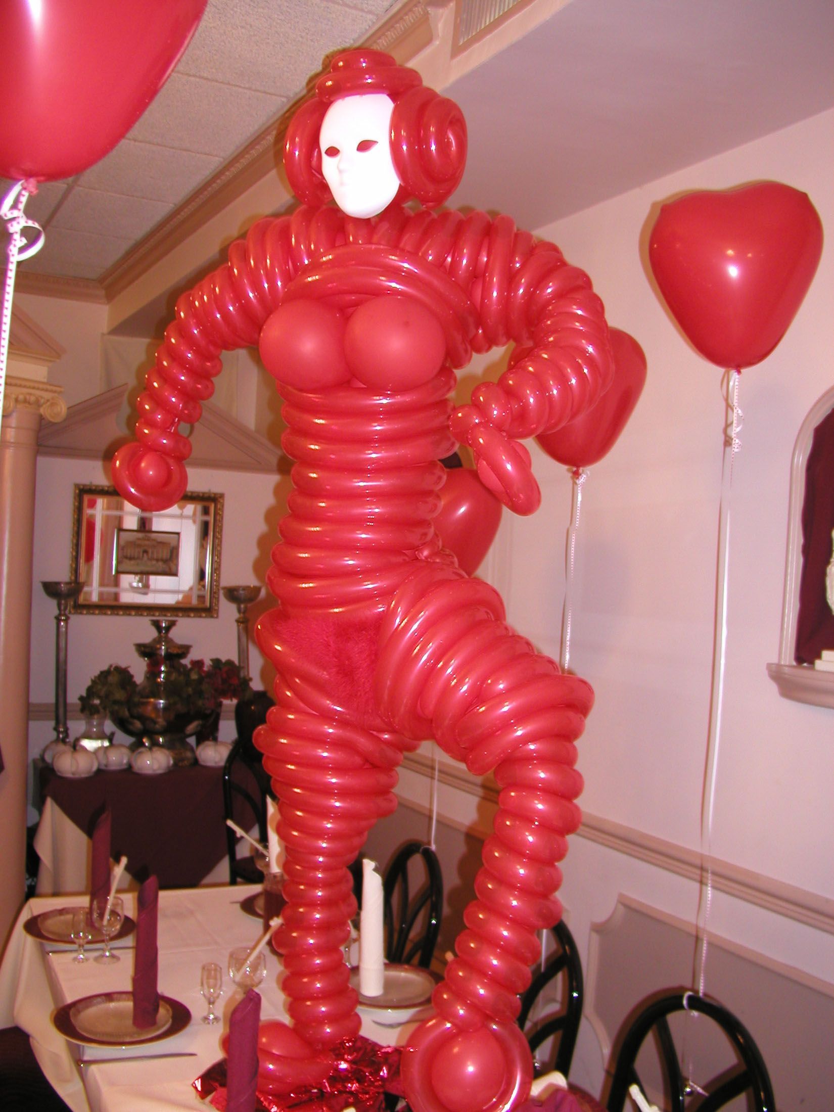 Red balloon sculpture of a person with a white mask, standing on a table with other decorations.
