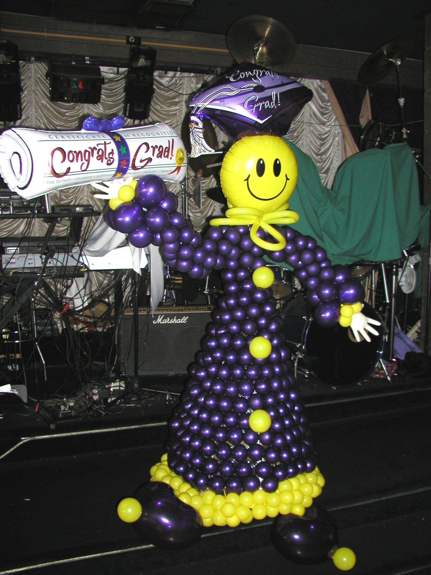 Balloon sculpture of a smiling figure in purple and yellow, holding a 