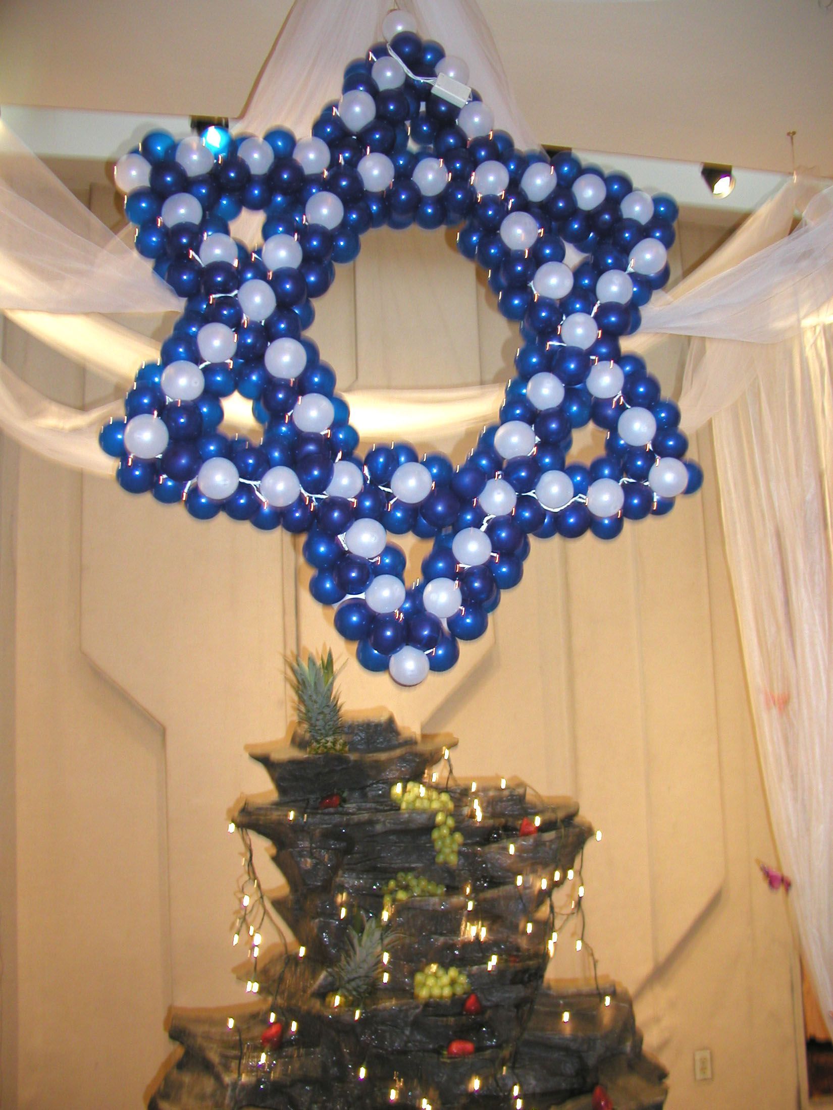 A Star of David made of blue and white balloons, above a tiered fountain.